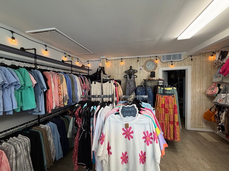 Interior of a colorful vintage clothing boutique with racks of garments, hanging displays, and a white shirt with pink flowers on a center table