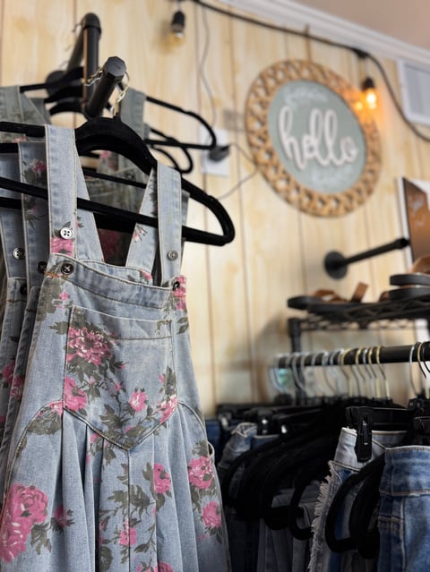 Floral denim apron hanging on black hooks with clothing racks and hello sign in background